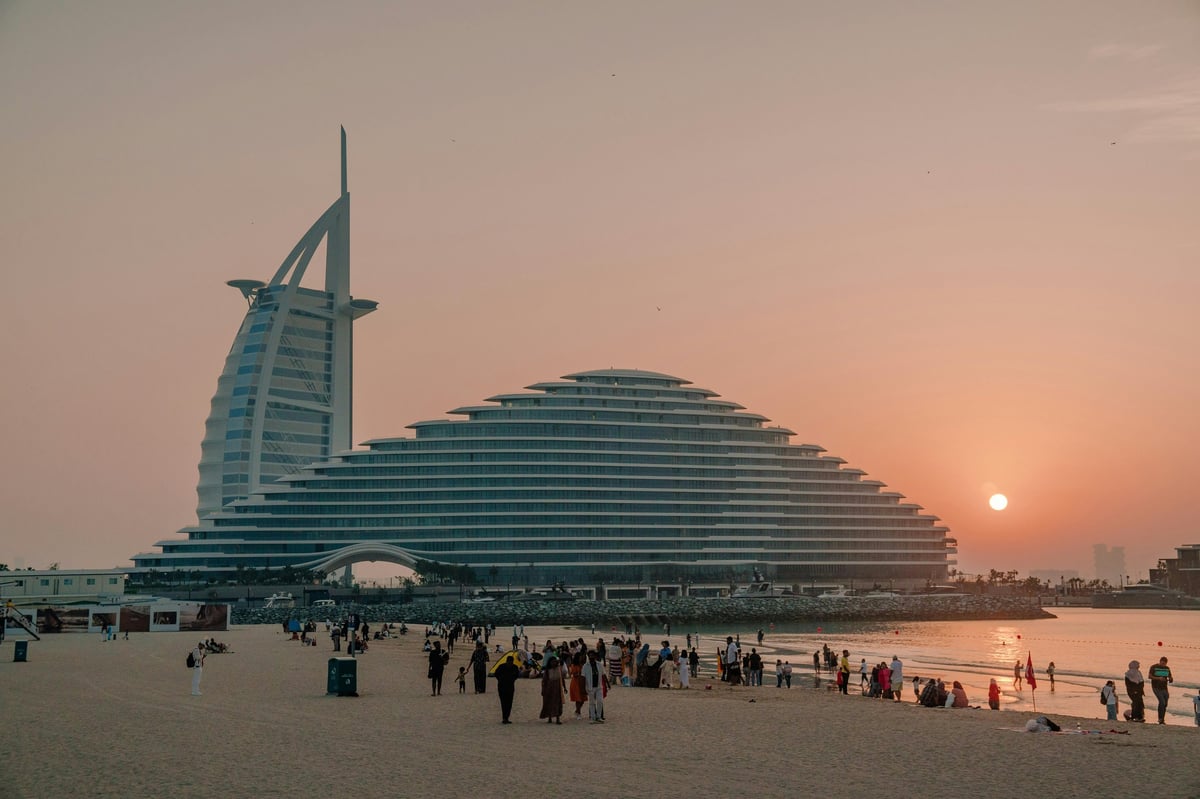 Burj Al Arab and Mina Al Salam hotel at sunset with crowds on beach and calm ocean water