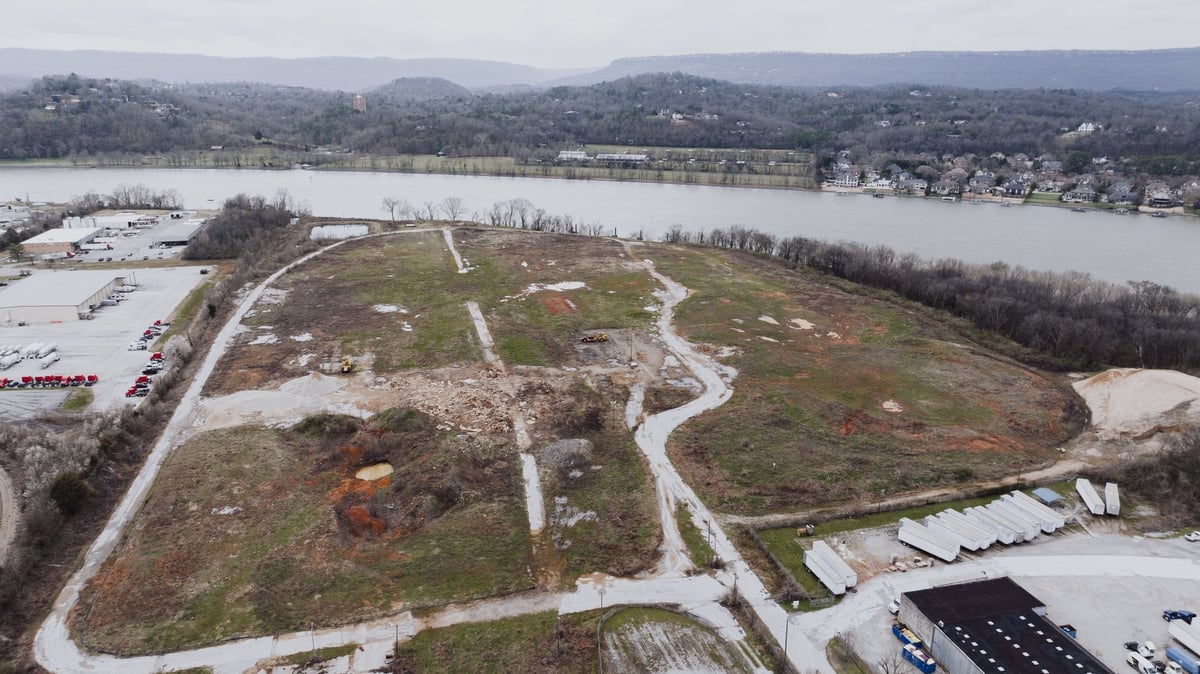 Aerial view of undeveloped land with winding paths, surrounded by flooded fields and industrial buildings near a river