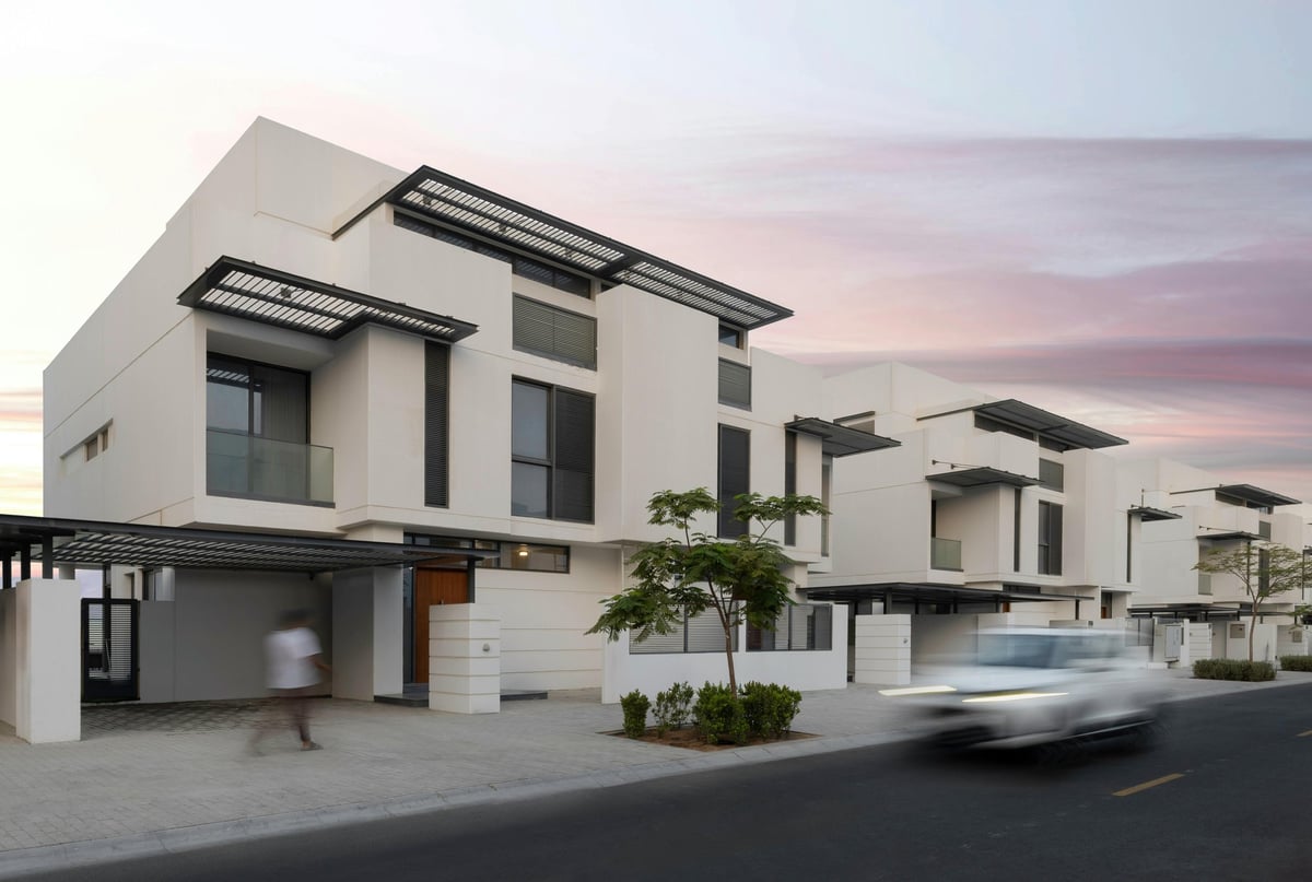 Modern white townhouses with solar panels, garage spaces, and landscaping along a residential street at dusk