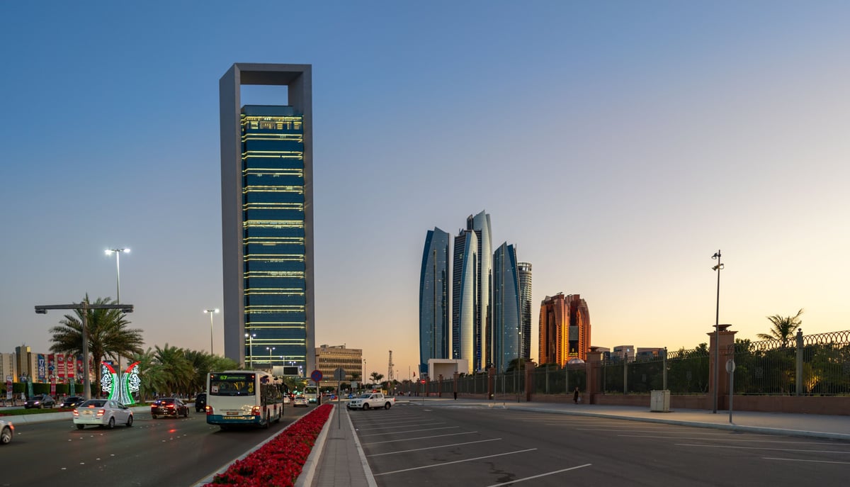 Modern cityscape with tall rectangular tower building and distinctive curved skyscrapers along wide street at dusk