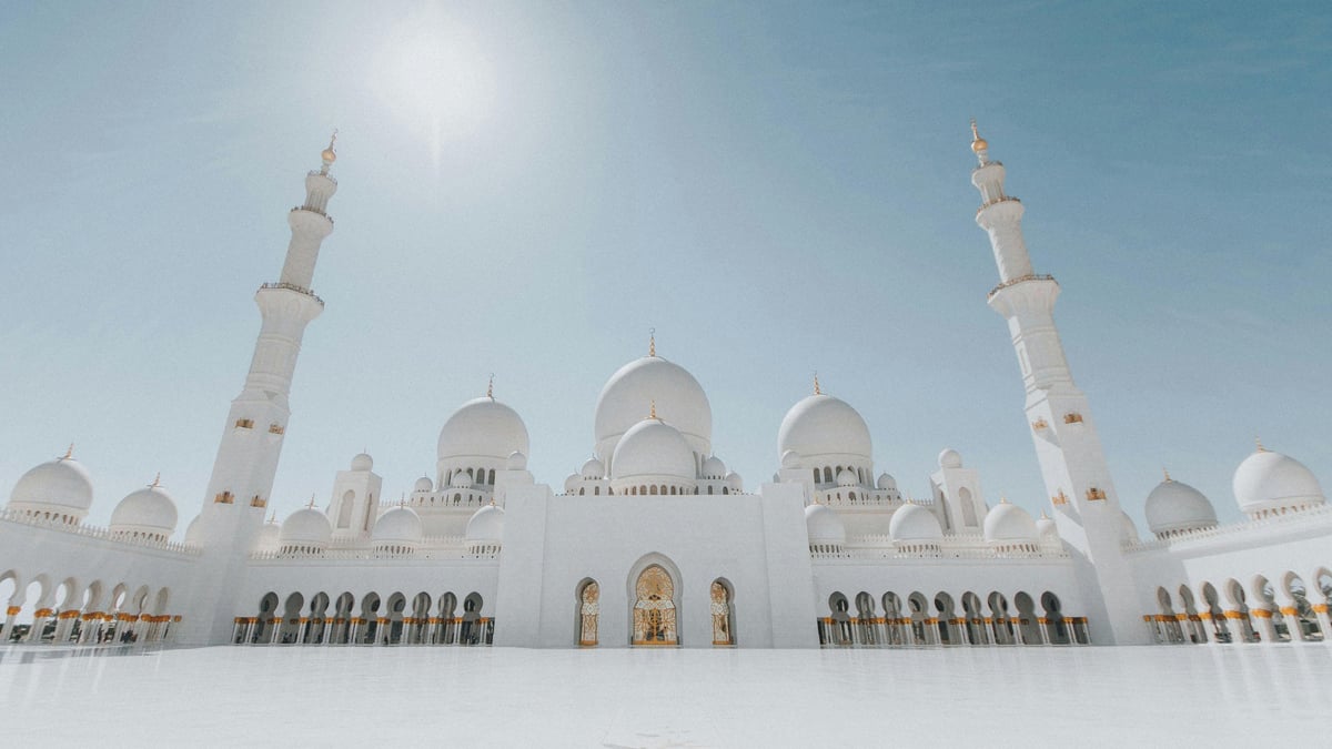White mosque with two tall minarets, domes, and arched colonnade under clear sky