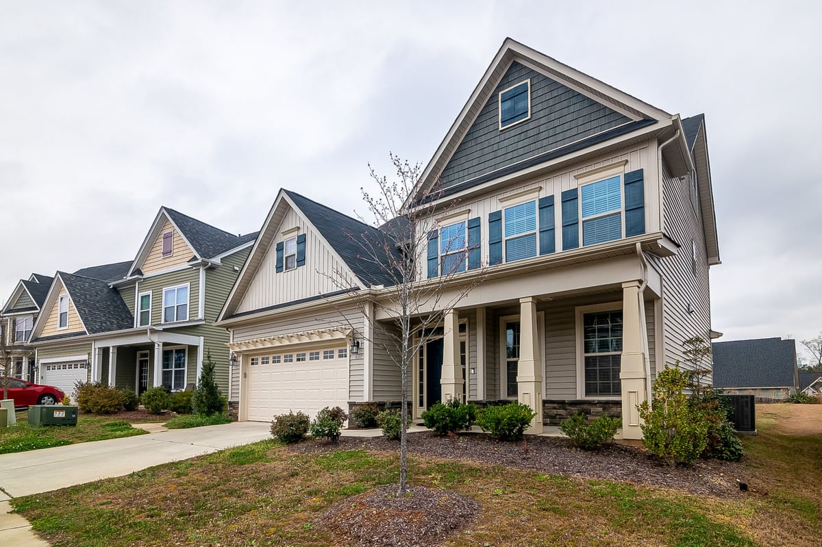 Two-story beige and gray residential home with attached garage and front landscaping on a suburban street