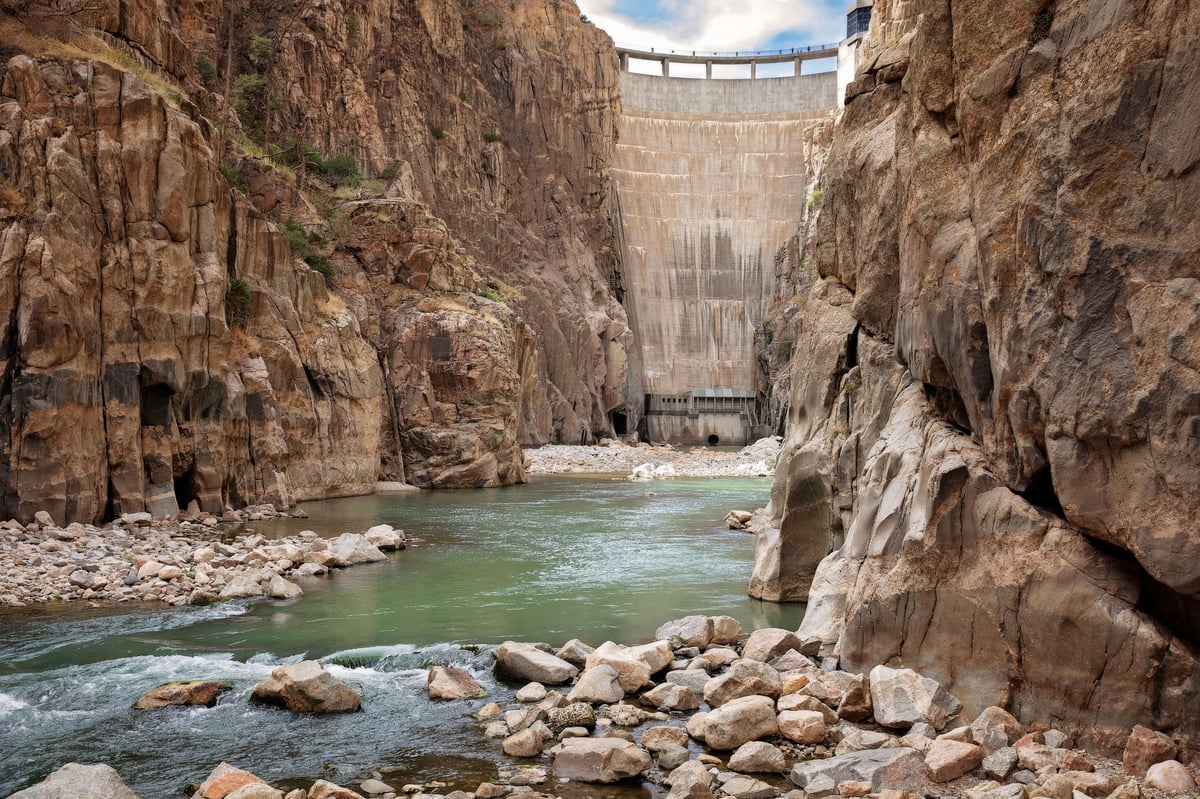 Concrete dam spanning a narrow canyon with turquoise river flowing through rocky gorge below
