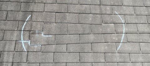 White chalk drawing on gray pavement showing a simple face with curved lines forming eyes and smile