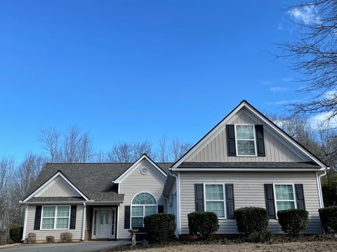 Two-story white suburban house with gable roof, blue sky, and bare trees in winter setting