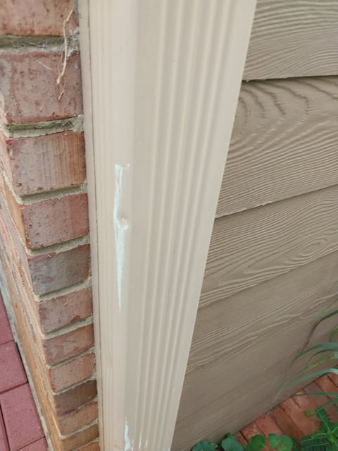 Cream-colored vinyl siding panel installed between red brick wall and beige textured siding on building exterior