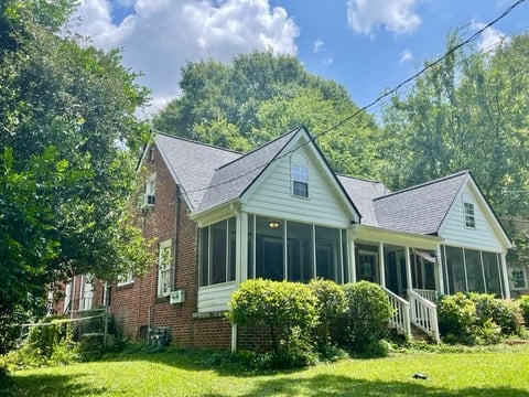 Two-story brick and siding house with screened porch surrounded by green lawn and trees under blue sky