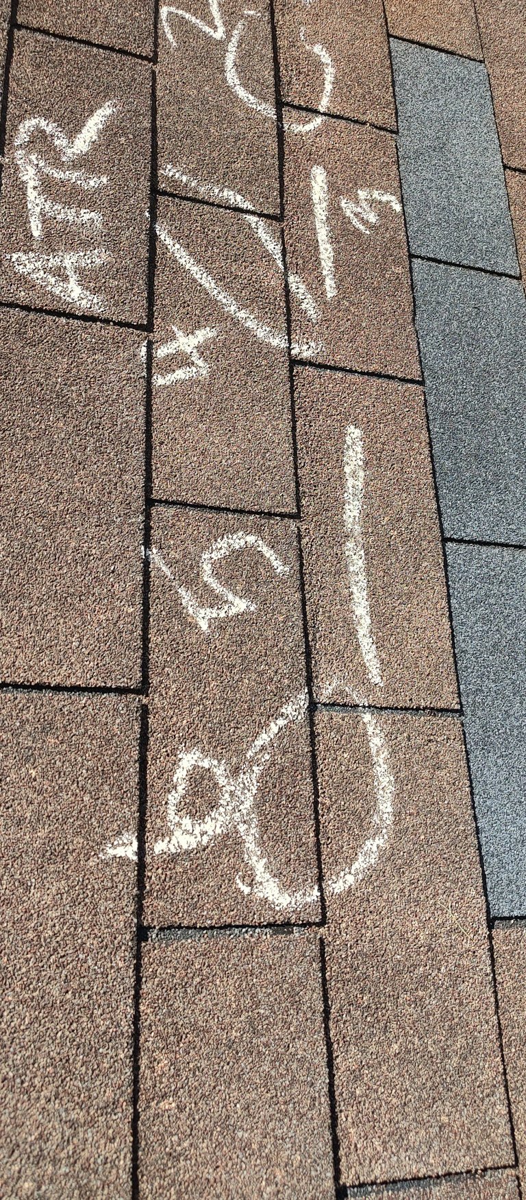 Close-up of asphalt shingles with white chalk markings and inspection codes on a roof