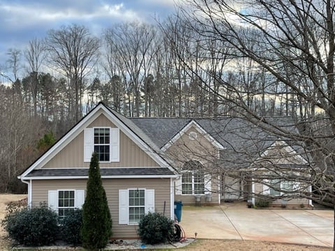 Suburban two-story house with white siding, gray roof, and bare trees in winter landscape setting