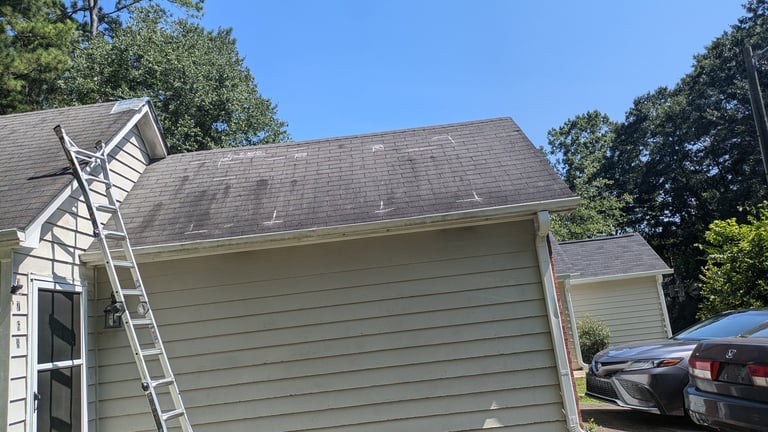 Exterior view of a residential house with gray siding, gray roof, and an extension ladder leaning against the garage wall near parked cars