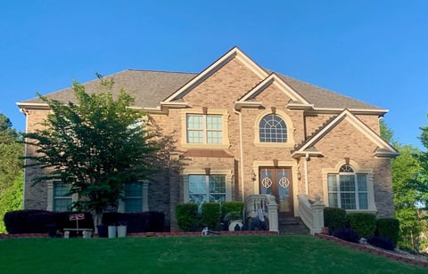 Two-story brick house with peaked roof, multiple windows, and manicured landscaping on a sunny day