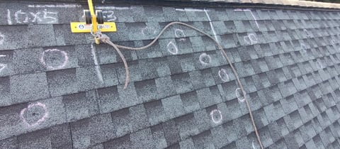 Yellow measuring cross on asphalt roof shingles with survey markings and measurement tape during roof inspection