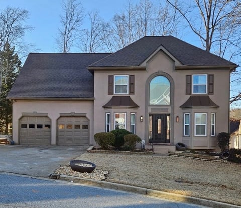 Two-story beige and brown residential home with two-car garage, large arched window, and driveway lined with landscaping
