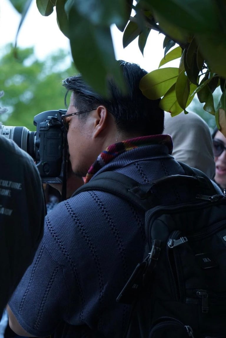 Person photographing tree foliage with professional camera, wearing dark jacket and red scarf