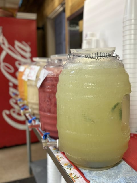 Glass jar filled with pale green liquid and mint leaves with a metal lid, displayed at a beverage counter with Coca-Cola branding visible
