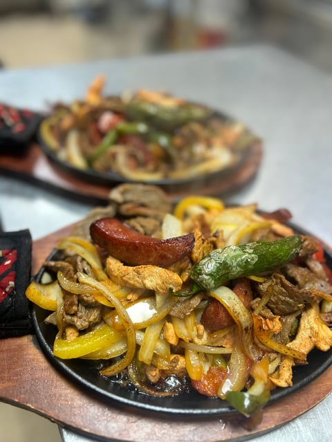 Sizzling fajitas on cast iron skillet with sliced meat, peppers, and onions served on wooden plate