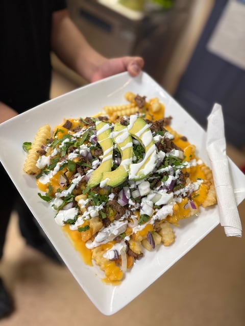 Person holding a white plate of loaded french fries topped with cheese, greens, and white crema sauce