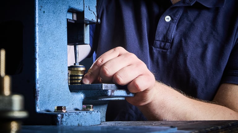 Workers hand operating a blue industrial press machine or lathe equipment in a workshop setting