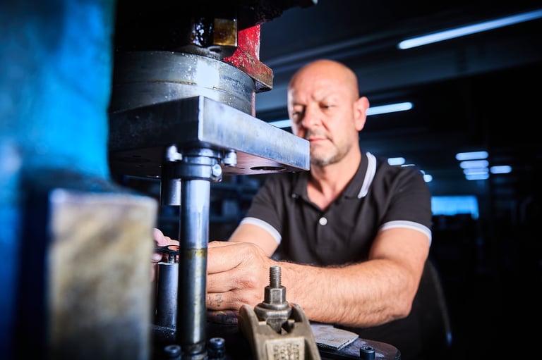 Man in black polo shirt operating industrial machinery in a workshop with blue lighting