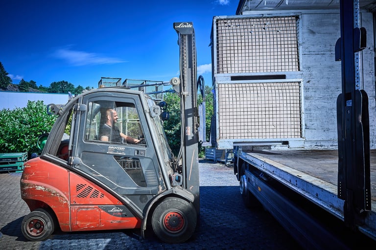 Red and gray forklift lifting a white crate onto a truck bed under clear blue sky