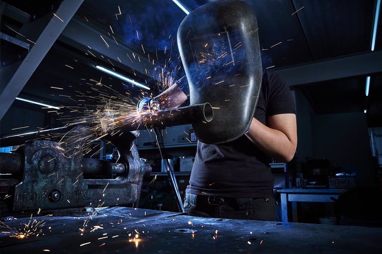 Welder in protective gear working on metal with sparks flying in an industrial workshop setting