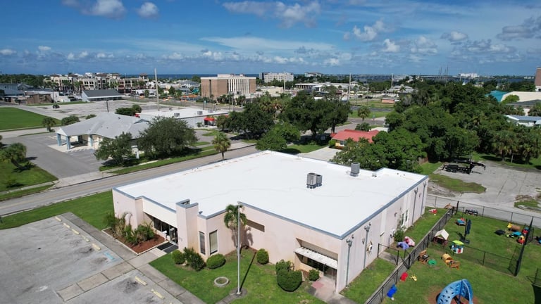 Drone view of a commercial building's white flat roof with low parapets and rooftop HVAC units