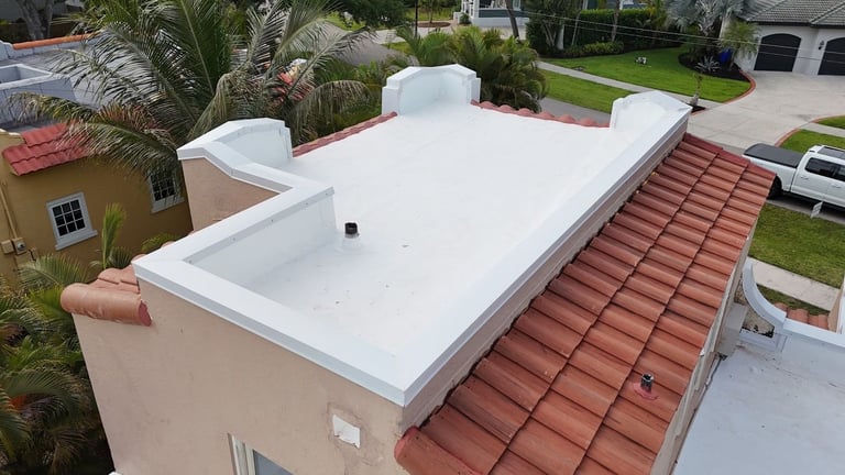 Close-up of a white flat roof membrane with white metal parapet coping, flashed pipe vent, and red clay barrel tile slope