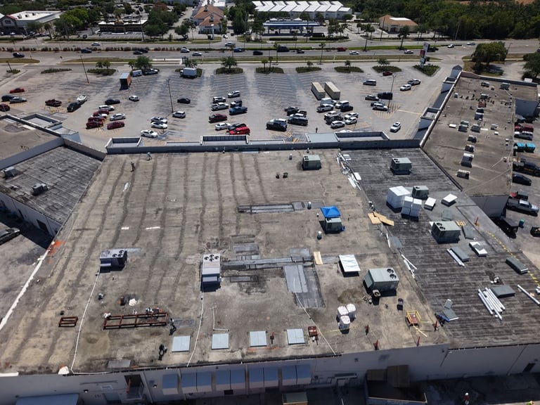 Aerial of a commercial flat roof replacement in progress on a retail store, old roof stripped around rooftop HVAC units