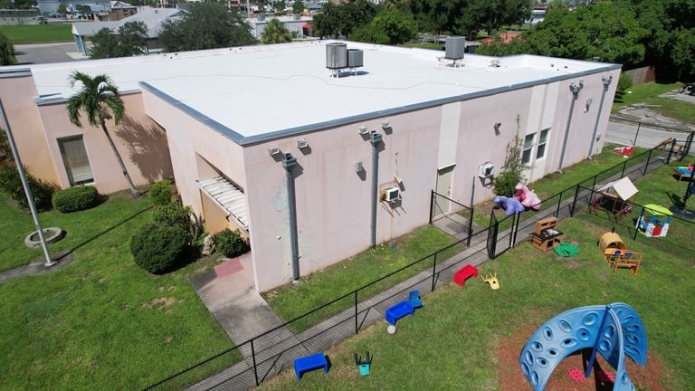 White flat roof with metal edge trim and HVAC units on a single-story day care building beside its playground