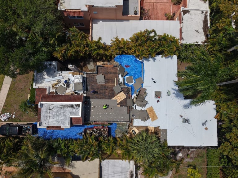 Top-down aerial of a flat roof replacement in progress, half covered in new white membrane and half in insulation board
