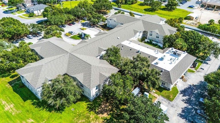Aerial of a two-story care facility wing with new gray architectural shingles and a white flat roof section