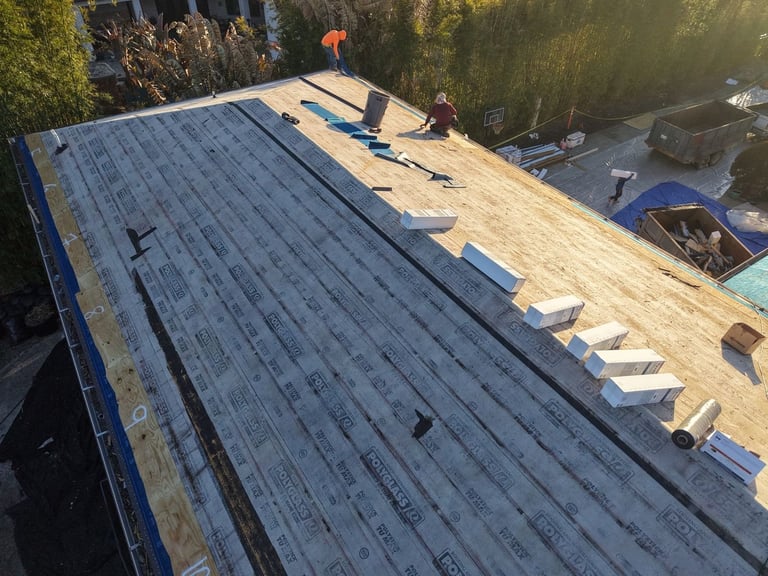 Self-adhered base sheet underlayment installed on a sloped roof deck with roofing supplies staged along the ridge