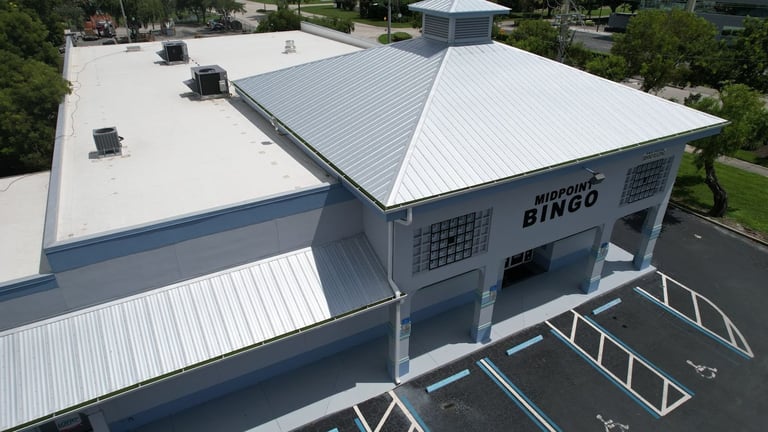 Aerial view of a bingo hall in Cape Coral, FL with a silver metal hip roof, cupola, metal canopy and white flat roof