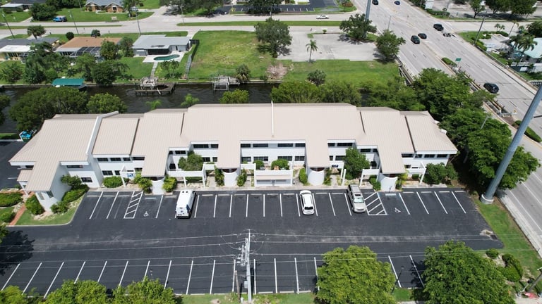 Aerial view of a commercial plaza and parking lot with a new tan standing seam metal roof in Cape Coral, FL