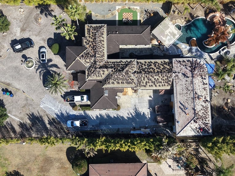 Top-down drone view of a tile roof replacement with old concrete tiles being lifted off across the home