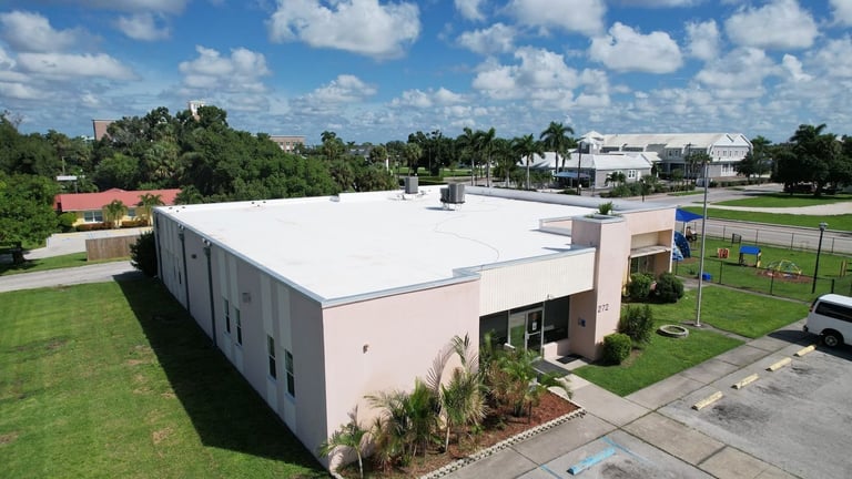 Aerial view of a day care center with a bright white flat roof, rooftop AC units and parapet edge metal