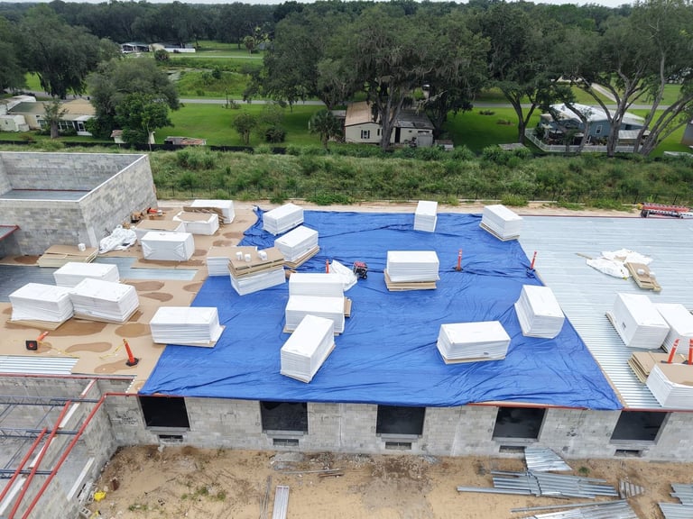 Aerial view of a commercial flat roof in Leesburg, FL, with insulation pallets staged on a protected steel roof deck