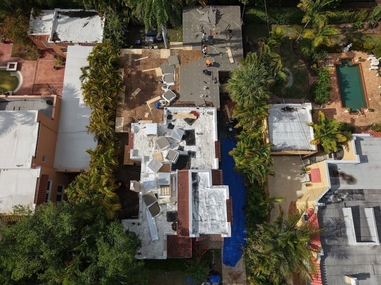 Overhead drone view of a flat roof tear-off on a home, old roof stripped to the deck with insulation boards going down