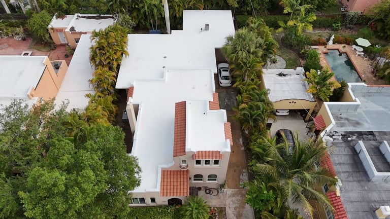 Wide aerial of a residential street showing a home's new white flat roof among neighboring tile roofs