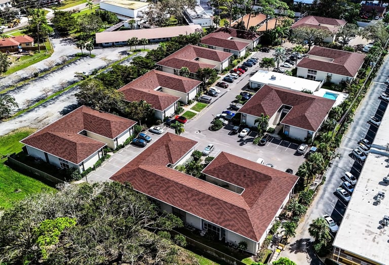 Angled aerial of two-story condo buildings with matching red-brown shingle roofs and a central parking lot