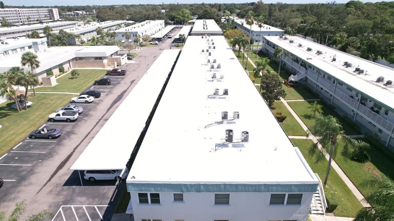 New white TPO roof on a long two-story residential building with rooftop AC units and covered parking