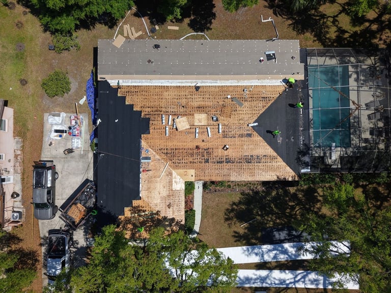 Overhead drone view of a home re-roof in progress: shingles torn off, new decking, underlayment and flat roof insulation