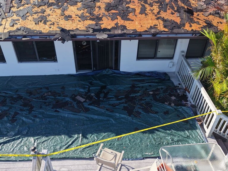 Tarp covering a backyard deck below a roof tear-off, with patio furniture and railing protected from debris