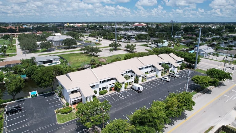 Wide aerial of a commercial building with a new standing seam metal roof beside a busy road in Cape Coral, FL
