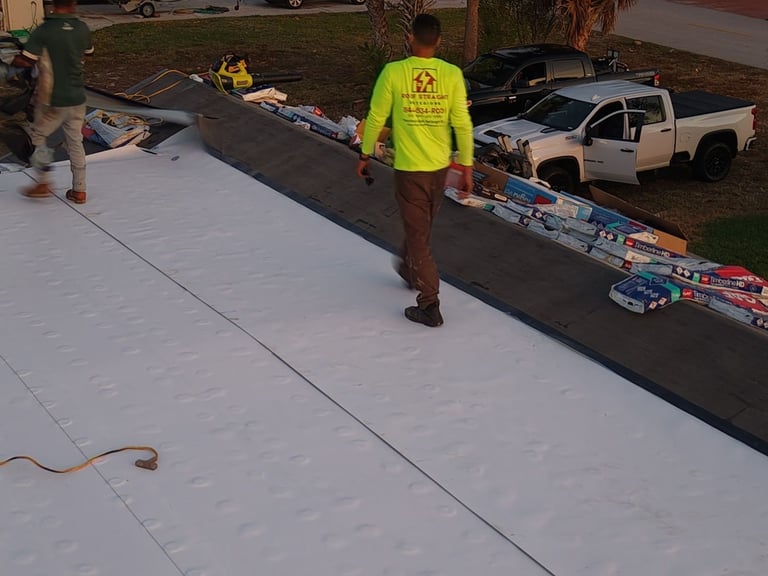 Roofer in a hi-vis company shirt walking on new white TPO flat roof next to a shingle slope with bundles staged