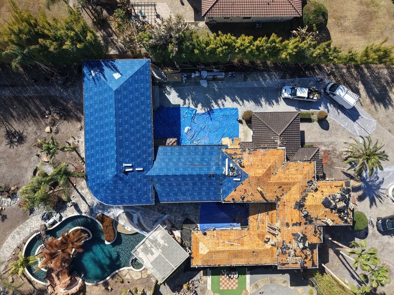Top-down aerial of a tile roof replacement with new blue underlayment on one wing and bare plywood deck on the other