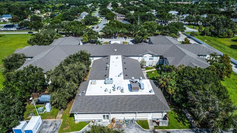Aerial of a senior living facility showing new gray shingle roofs around a white low-slope flat roof
