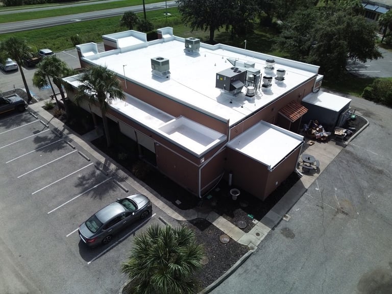 Side aerial view of a restaurant's finished white flat roof with parapet walls and rooftop equipment