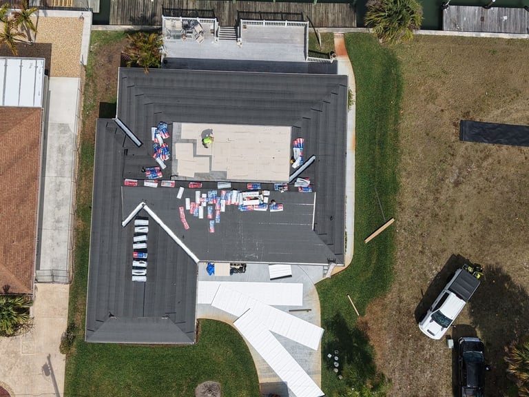 Overhead drone view of a hip roof with new underlayment, GAF shingle bundles staged and cover board on the flat roof section