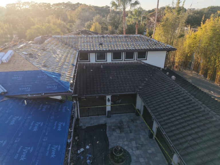 Old tile roof section beside new blue self-adhered underlayment during a tile roof replacement